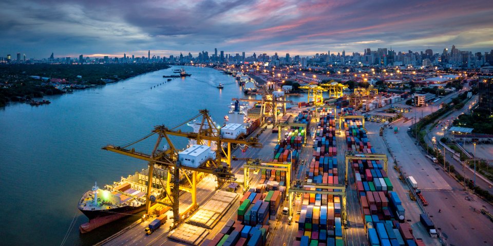 Aerial view of international port with Crane loading containers in import export business logistics with cityscape of Bangkok city Thailand at night 