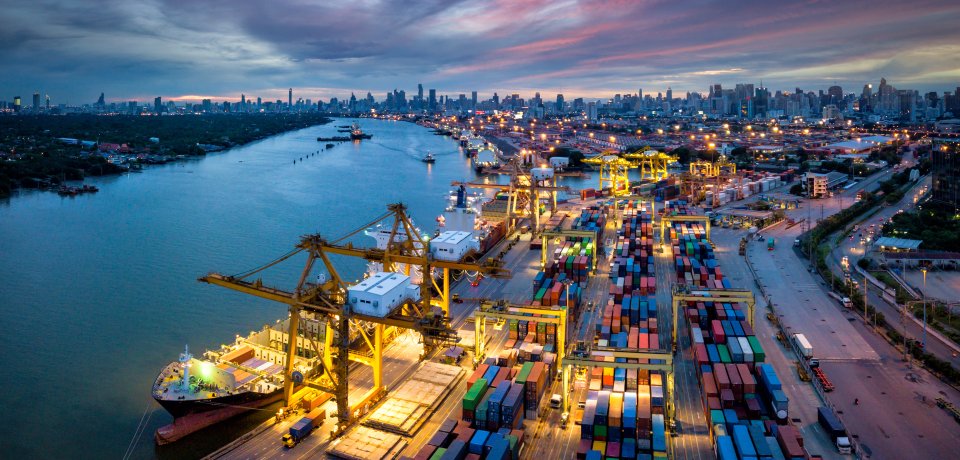 Aerial view of international port with Crane loading containers in import export business logistics with cityscape of Bangkok city Thailand at night 